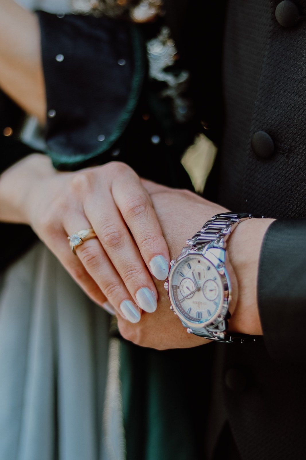 Bride's hand with engagement ring resting on the groom's watch