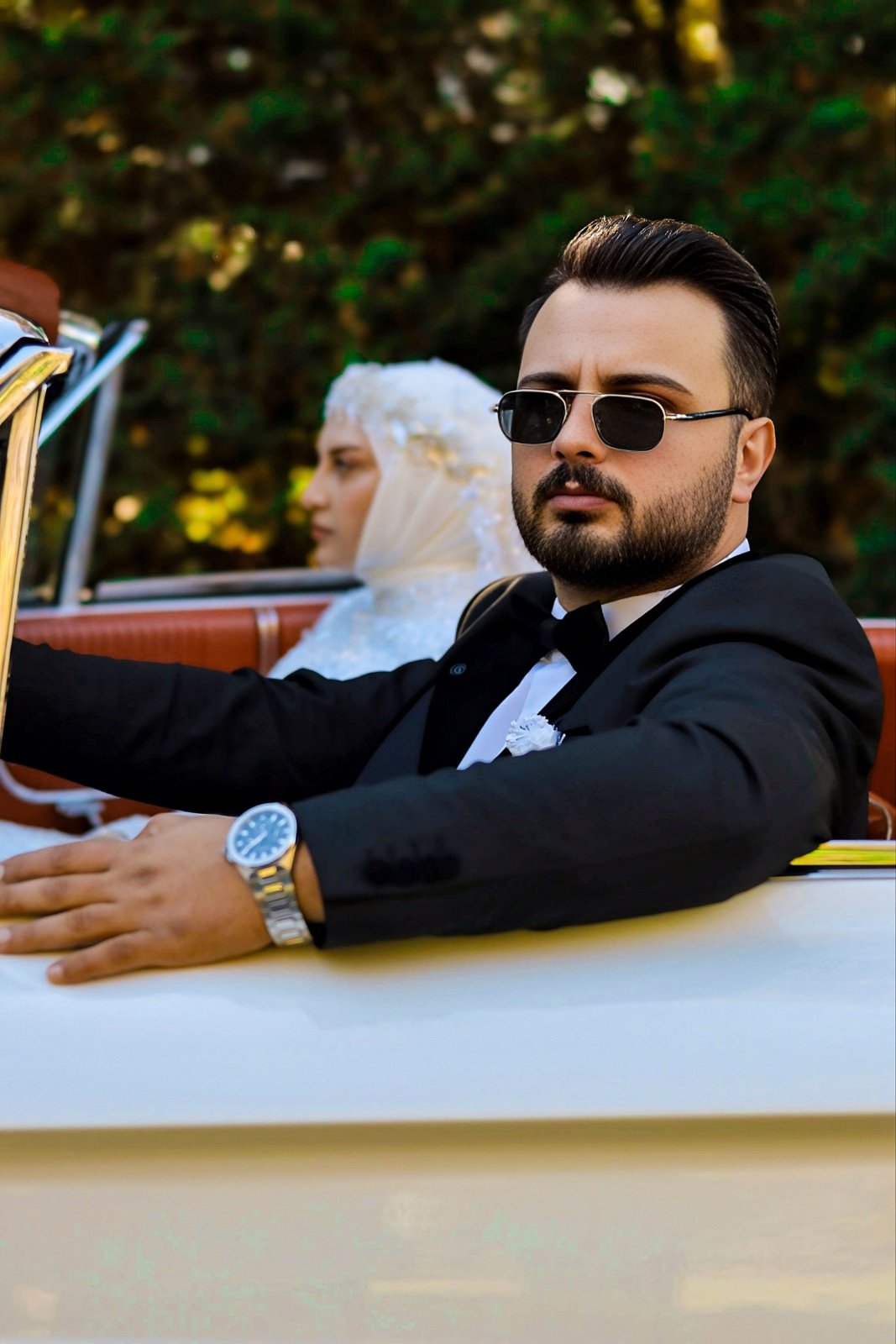 Groom in sunglasses at the wheel of a vintage convertible